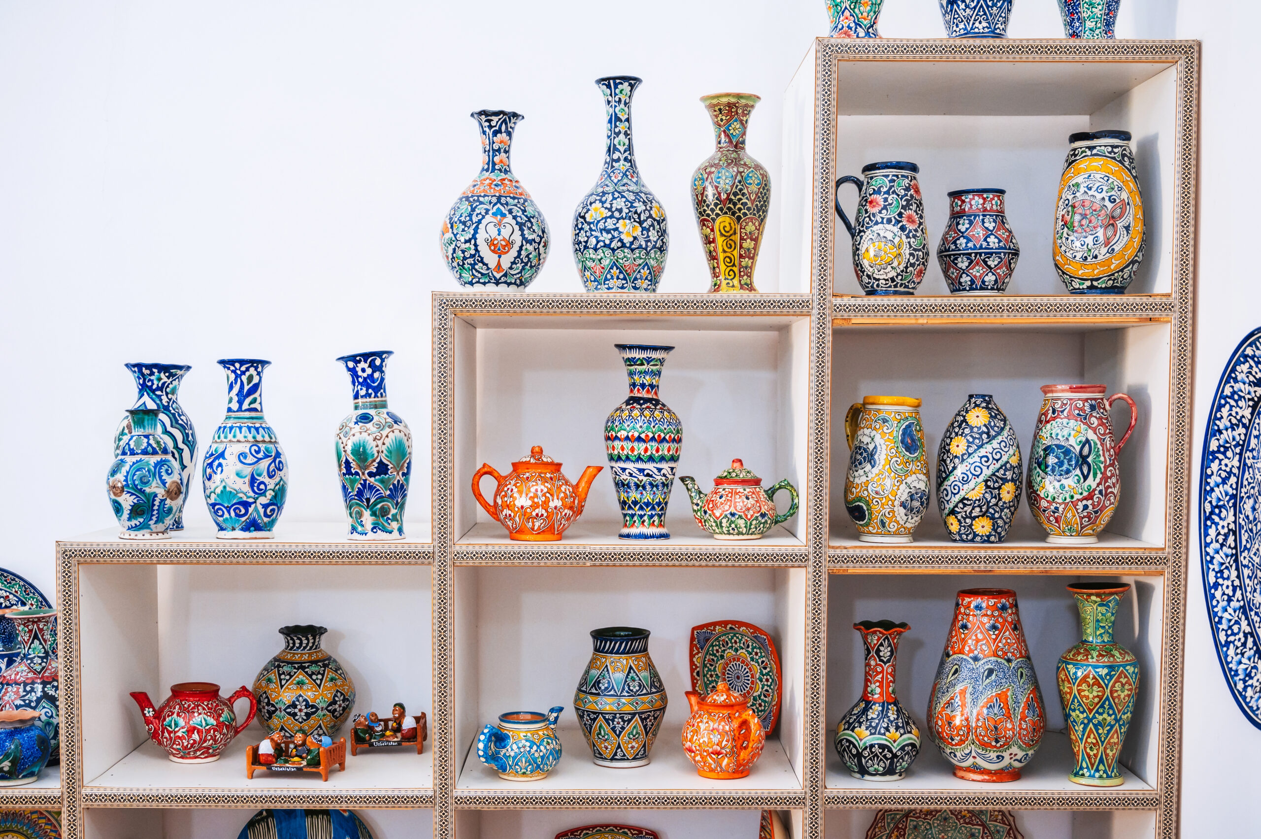 Uzbek ceramic vases with hand-painted traditional Asian colorful patterns on shelves on a white background